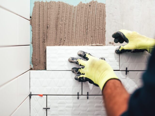 Tegelzetter plaatst witte wandtegels met tegelkruisjes