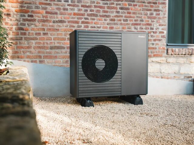 Buitenunit van een lucht-water warmtepomp naast een bakstenen woning