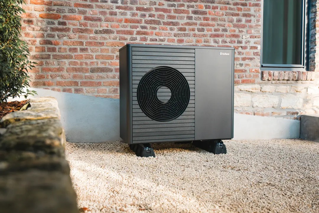 Buitenunit van een lucht-water warmtepomp naast een bakstenen woning